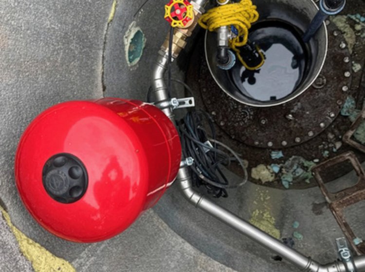 Blick in eine Zisterne von oben. Man sieht einen roten Tank, Rohre führen in ein offenes Behältnis.