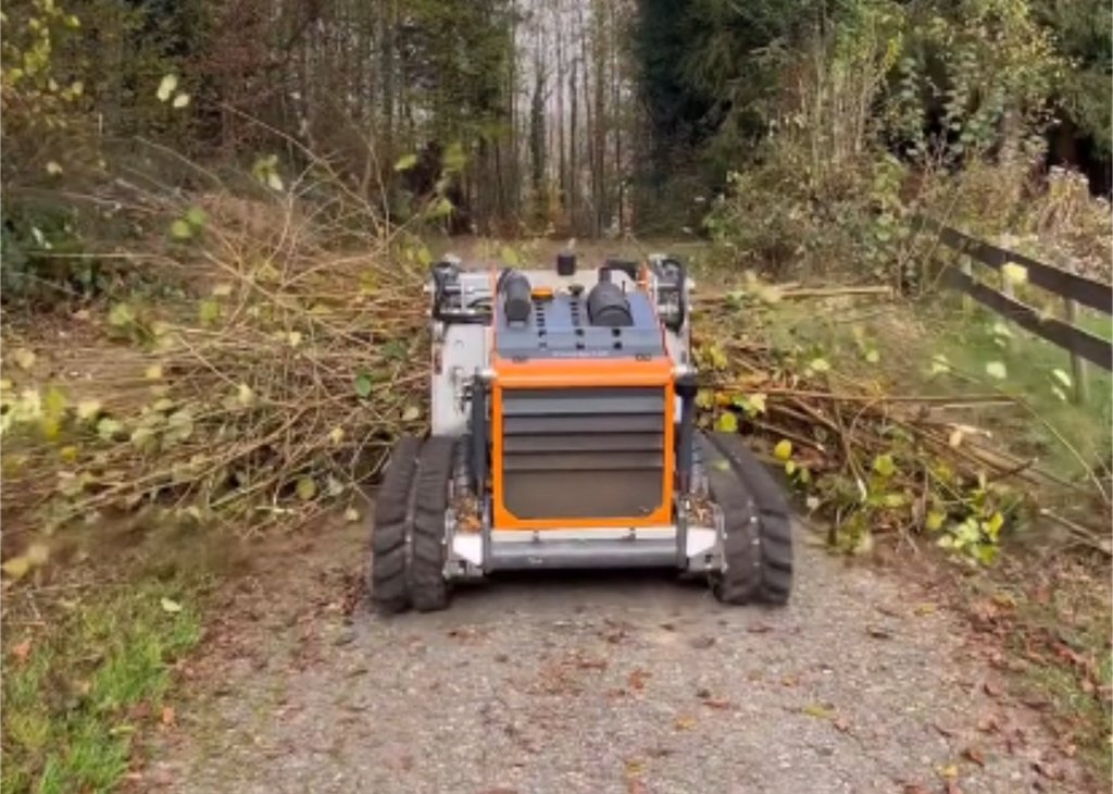 Ein kompakter Holzhäcksler auf Raupenfahrwerk zerkleinert Äste auf einem Waldweg, umgeben von hohen Bäumen im Herbst.