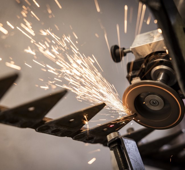 Eine vollautomatische Schleifmaschine, die das Messer eines Balkenmähers. Dabei sprühen Funken in den Raum.